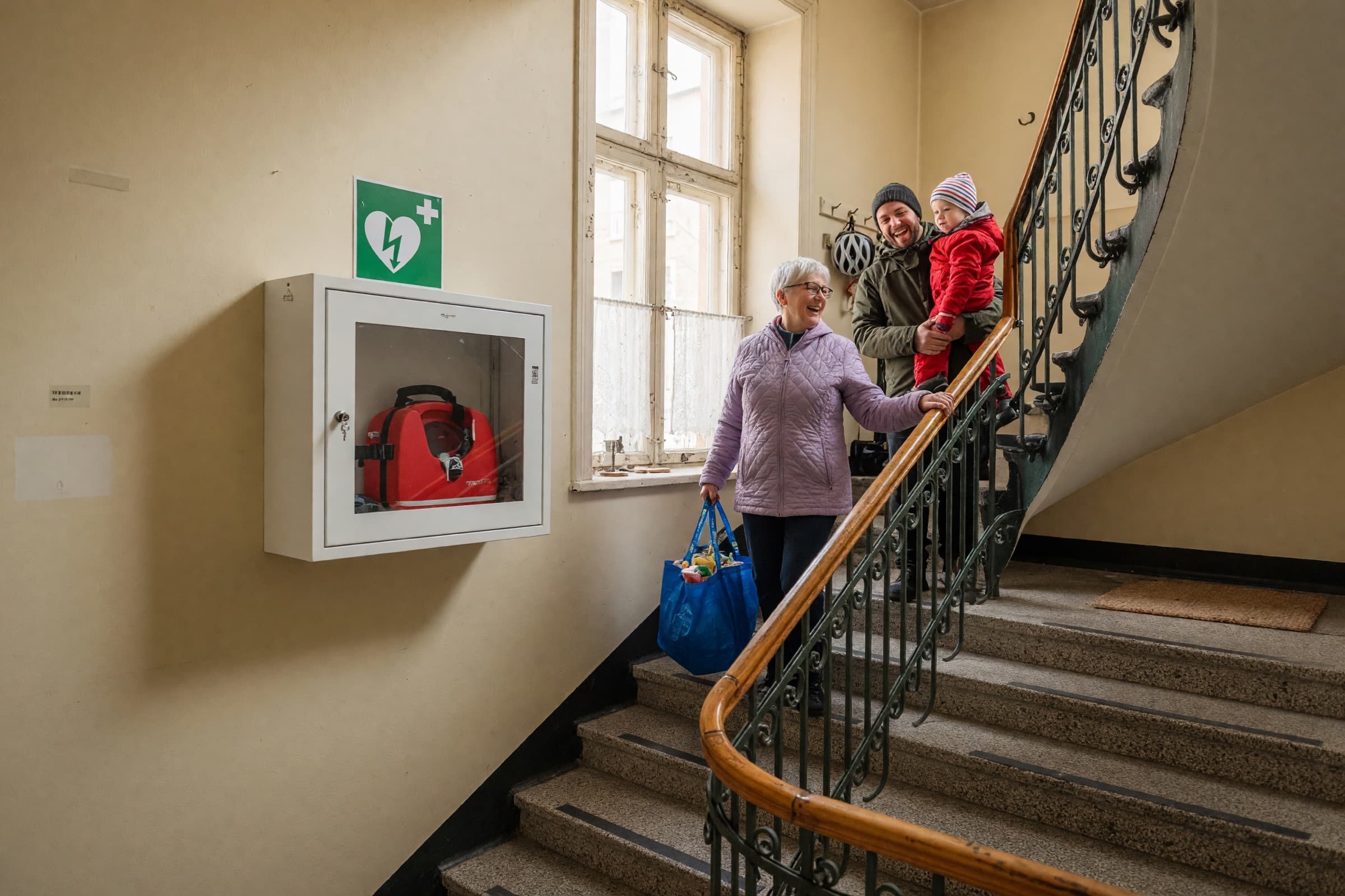 Grannar som möts i trappuppgången, med föreningens hjärtstartarskåp på väggen