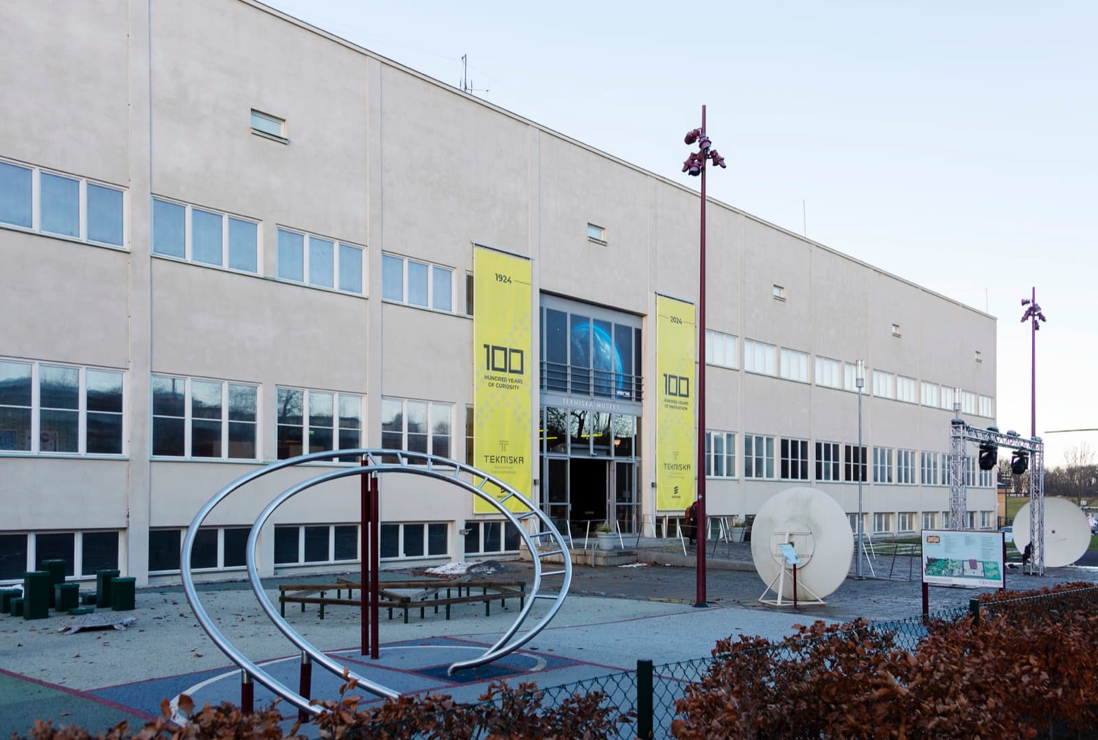 Tekniska museets fasad med jubileumsbanderoller och en skulptur i förgrunden