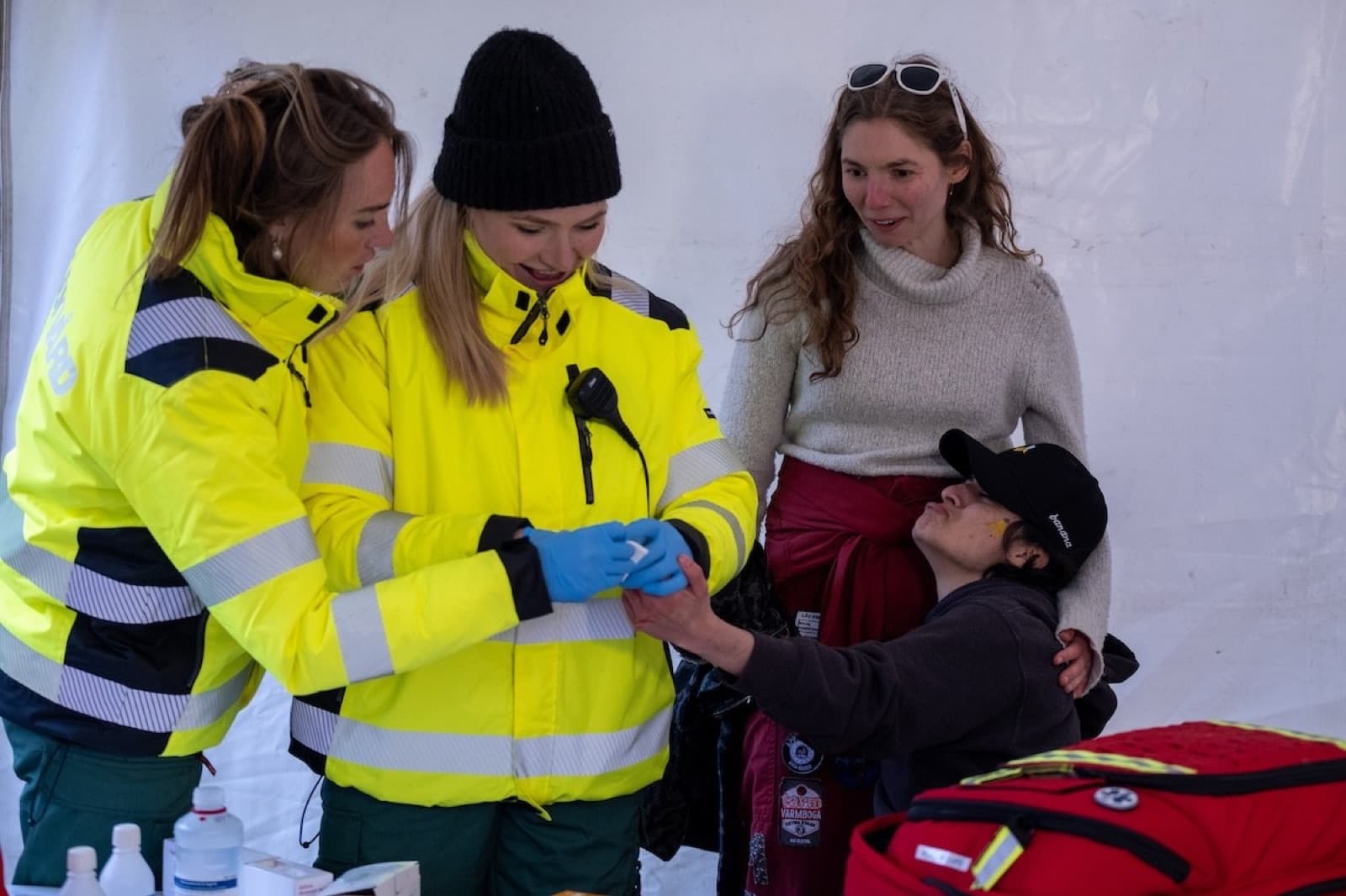 Sjukvårdspersonal i gula reflexjackor hjälper en person i ett vitt tält