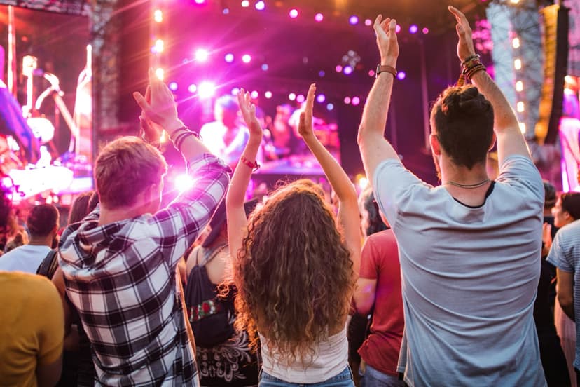 Publik med händerna i luften på en konsert med färgglada scenljus i bakgrunden