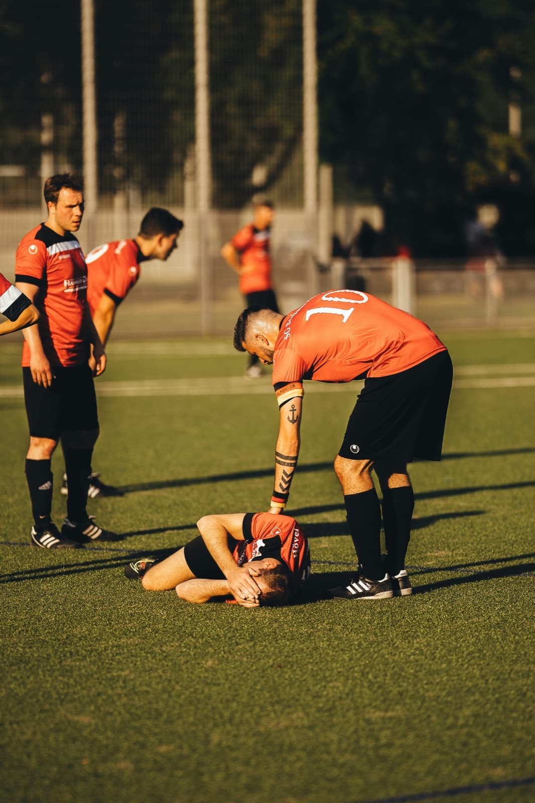 En fotbollsspelare ligger på planen och håller sig om huvudet medan en lagkamrat böjer sig över