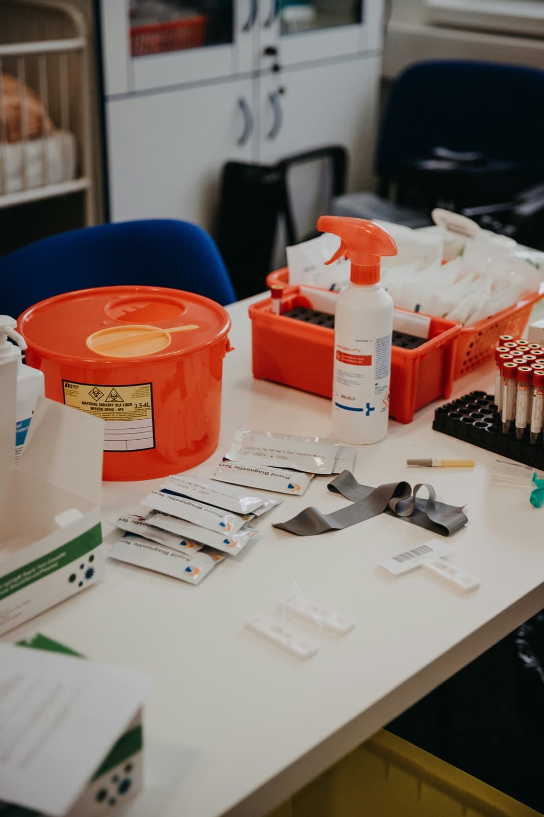 Ett skrivbord med en röd riskavfallsbehållare, testremsor och medicinska förpackningar i ett undersökningsrum