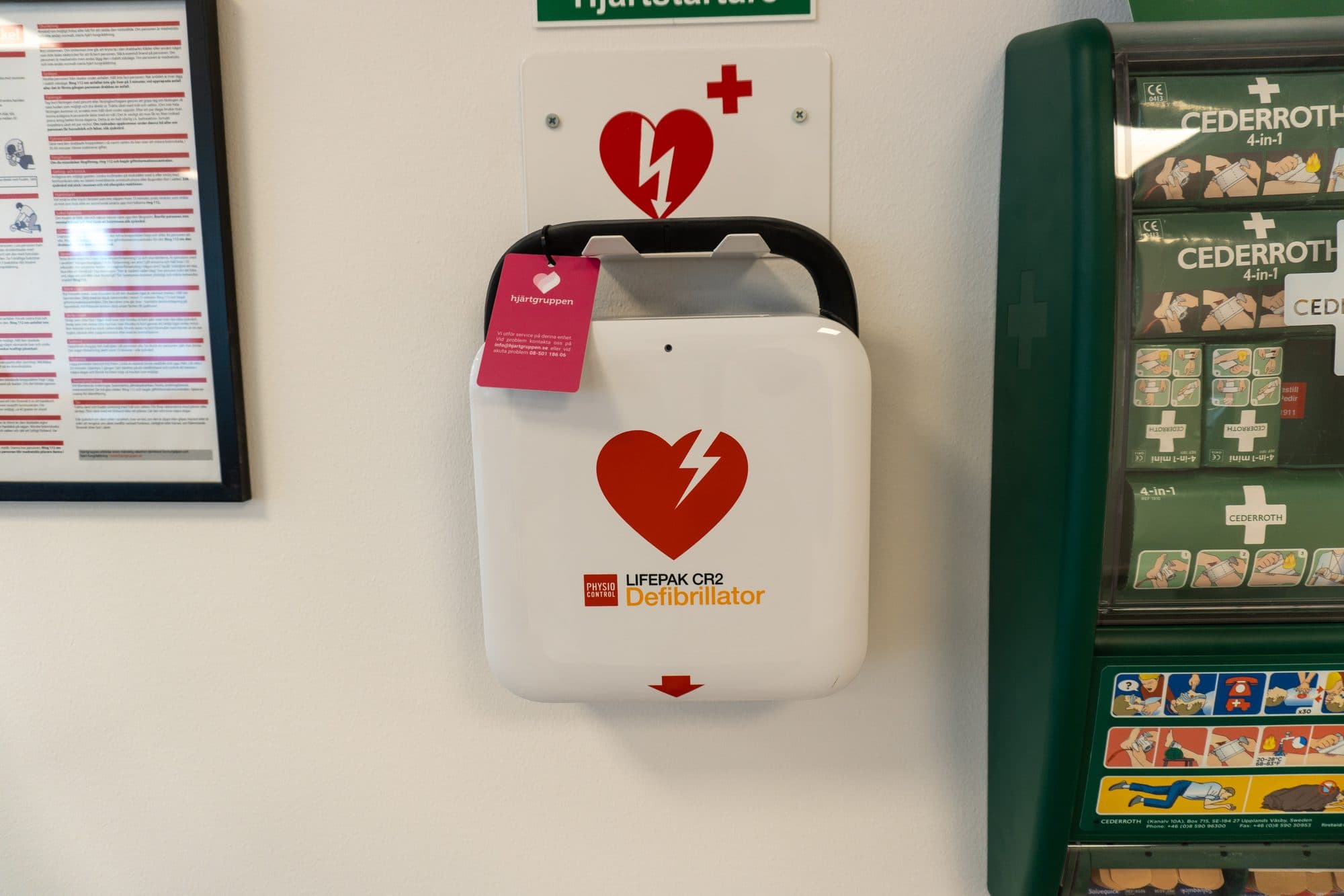 Vit hjärtstartare på en vägg bredvid en tavla med första hjälpen-material