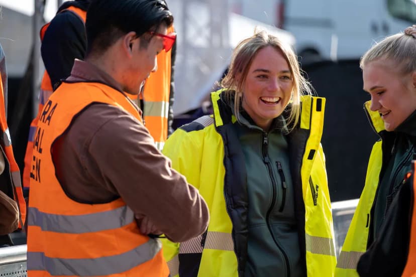 Personal i varselkläder samtalar och ler vid ett avspärrat område